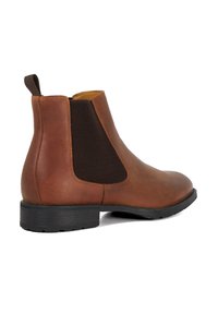 Brown leather Chelsea boot featuring elastic side panels, a pull tab, and a black rubber sole with textured tread.