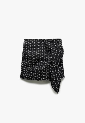 Czarna spódnica z tkaniny z białym wzorem kwiatowym, z detalem w postaci węzła z przodu i lekko teksturowaną powierzchnią, co podkreśla jej design.
