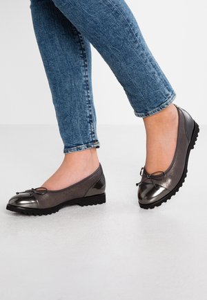 Mørkegrå flade sko med en skinnende tåhætte, en sløjfedetalje og en tekstureret sål. Bruges med blå jeans og viser et lavprofildesign.