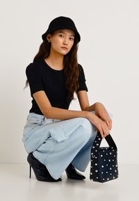 Černý přiléhavý top, světle modré džíny s širokými nohavicemi, černé lodičky na jehlovém podpatku, černý klobouk typu bucket a strukturovaná černá kabelka se stříbrnými nýty.