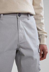 Pantalones cargo de color gris claro con una textura suave, bolsillo lateral y cierre de botón. Combinados con un suéter de punto color crema.