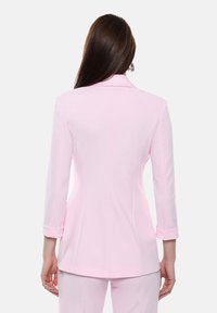Blazer rosa chiaro con una vestibilità su misura, colletto strutturato e maniche a tre quarti. Tessuto morbido con una leggera lucentezza e cuciture curate.