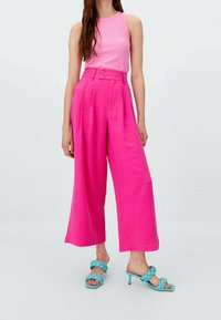 Różowa, krótka bluzka na ramiączkach w połączeniu z różowymi, wysokimi spodniami o szerokich nogawkach oraz błękitnymi sandałami na obcasie z plecionymi akcentami.