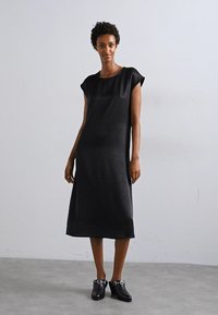 Black, short-sleeve dress with a relaxed fit and knee-length hem. Made of lightweight fabric with a smooth texture. Worn with black shoes.