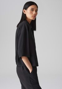 Top corto nero a maniche corte, largo e abbinato a pantaloni, con una silhouette rilassata e un tessuto morbido, dotato di tasche laterali e un design pulito e minimal.
