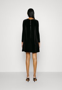 Zwarte fluwelen jurk met lange mouwen, A-lijn vorm en ritssluiting aan de achterkant. Soepele textuur en minimalistisch ontwerp.