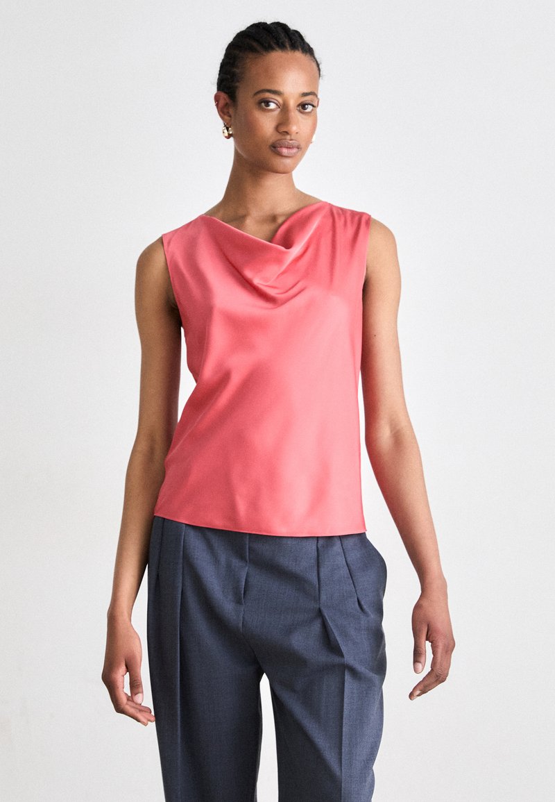 Κοραλί σατινένιο τοπ χωρίς μανίκια με ντραπέ λαιμόκοψη, συνδυασμένο με κομμένα ναυτικά παντελόνια με πιέτες και τσέπες. Λείος υφασμάτινος στρόγγυλος.