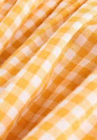 Tissu vichy jaune et blanc avec une texture tissée visible et des plis doux créant des ombres légères.