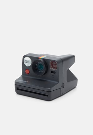 Polaroid Sofortbildkamera mit mattschwarzer Oberfläche, rundem Objektiv, Blitz, rotem Auslöser und einem Regenbogen-Akzentstreifen an der Oberseite.