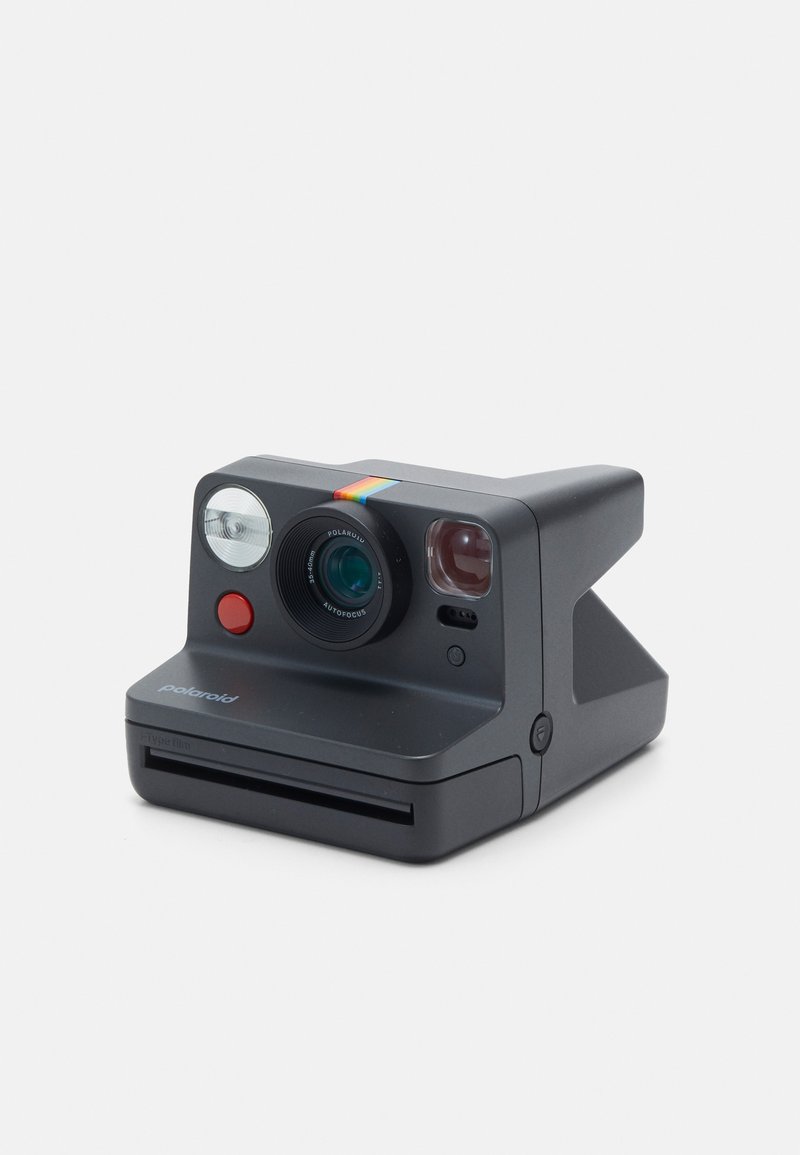 Polaroid instant camera with a matte black finish, round lens, flash, red shutter button, and a rainbow accent stripe on the top.