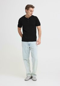 Polo noir à manches courtes avec col, patte de boutonnage à deux boutons, associé à un jean droit bleu clair et des baskets grises.