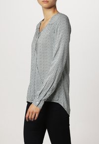 Czarna i biała w kratkę bluzka z długim rękawem, dekoltem w kształcie litery V, z listwą guzikową i lekko zaokrąglonym hemem. Lekki materiał o gładkiej teksturze.