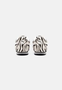Sapatilhas Puma com um padrão de zebra preto e branco, apresentando uma ponta arredondada e detalhes do logótipo no calcanhar e na lateral. Exterior em tecido suave.