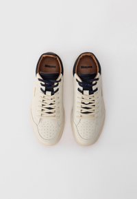 Biele kožené tenisky s tmavomodrými detailmi, perforovanou časťou na prstoch a béžovou gumovou podrážkou. Majú ploché šnúrky a vyrazené logo na boku.