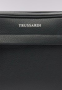 Czarna torebka ze strukturą z teksturowanej skóry, z zamkiem błyskawicznym, z poziomą kieszenią i wytłoczonym srebrnym logo "Trussardi".
