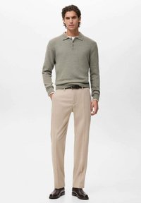 Maglione polo in misto lana verde con polsini a coste, abbinato a pantaloni beige su misura e scarpe in pelle marrone scuro. Design semplice e strutturato.