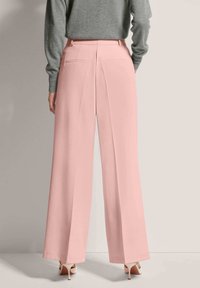 Roze wijde pijpen met een getailleerde pasvorm, met een zachte textuur en twee achterzakken. Gepaarde met lichtgekleurde hoge hakken.