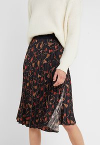 Plisserad kjol i svart tyg med ett färgglatt franje-mönster i röd, guld och brunt, med en slät textur och elastisk midja.