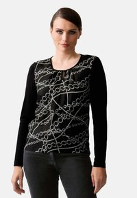 Langarm-Top mit einem schwarz-weißen Kettenmuster auf einem strukturierten Stoff, rundem Halsausschnitt und einem dezenten Schlitzdetail auf der Vorderseite.