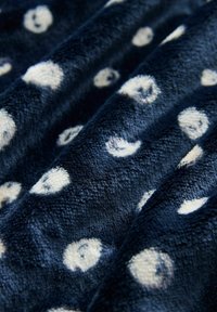 Tamsiai mėlynas aksominis audinys su baltais taškeliais, minkšta tekstūra ir šiek tiek blizgiu paviršiumi. Raštas tolygiai paskirstytas.