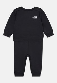 Ensemble noir deux pièces comprenant un haut à manches longues avec un col rond et un pantalon assorti avec une ouverture au niveau des pieds. Logo affiché sur la poitrine.