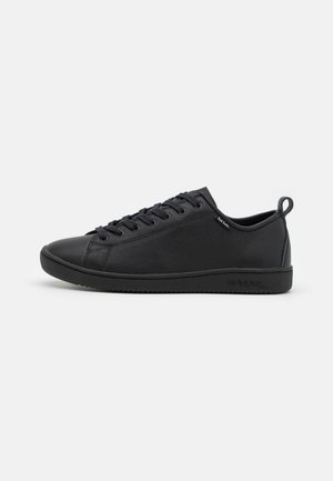 Zapatillas negras con parte superior de cuero suave, puntera redondeada, cordones en tono y suela de goma texturizada. Incluye una pequeña lengüeta en el talón.