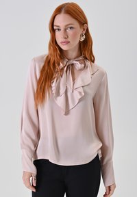 Helle rosa Satinbluse mit Rüsche am Kragen und Schleifen-Detail. Verfügt über lange Ärmel und einen abgerundeten Saum. Glatte Textur, schlichtes Design.