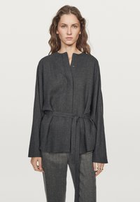 Blusa grigia scura dalla vestibilità morbida, con scollatura rotonda e una cintura da annodare in vita. Realizzata in un tessuto morbido con una leggera texture.