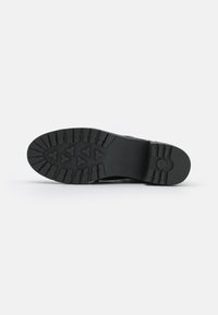 Semelle en caoutchouc noire avec des crampons épais et des rainures bien définies ; design plat adapté à la traction. Aucun motif ou accent visible.