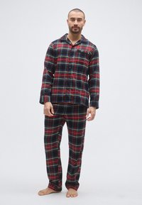 Męski zestaw piżam w kratę w kolorach czarnym, czerwonym i zielonym. Miękka tkanina, koszula zapinana na guziki oraz spodnie z elastycznym pasem i kieszonką.