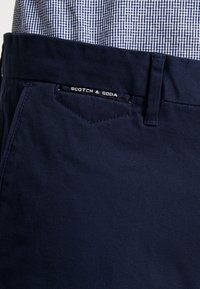 Marineblå bomuldsbukser med et elegant fit, med en subtil tekstur og en synlig logoetiket med teksten "SCOTCH & SODA" på linningen.