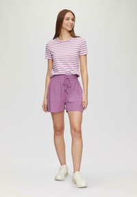 T-shirt rayé violet avec un col rond associé à un short lavande avec une taille élastique et deux poches latérales. Chaussures de sport.
