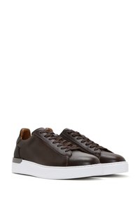Une paire de baskets basses en cuir marron foncé avec des lacets foncés et des semelles en caoutchouc blanc épais, isolées sur un fond blanc.