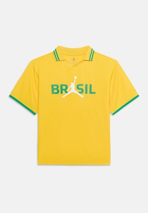 Sárga rövid ujjú galléros póló zöld szegéllyel, „BRASIL“ felirattal és egy fehér sziluettel, amelyen egy kosárlabdázó látható középen, aki labdát tart.