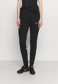 Schwarze Sporthosen mit tapered Fit, elastischem Bund und weißem Nike-Logo. Hergestellt aus leichtem Material, mit Seitentaschen.