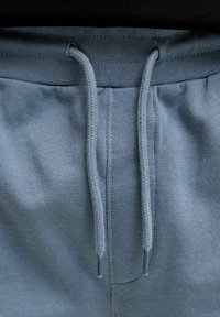Gros plan sur la taille d'un pantalon de survêtement bleu avec un cordon noué, montrant la texture du tissu tricoté et les détails de la couture.