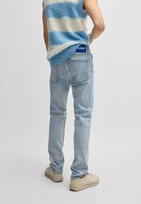 Jeans azzurri chiari in denim, stile aderente, design a cinque tasche. Abbinati a un top senza maniche a righe in maglia e calzature color beige.
