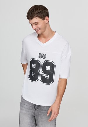 T-shirt bianco con scollatura a V e maniche corte, caratterizzato da una stampa grafica nera del numero "89" e della scritta "Eagle View". Il tessuto appare liscio.
