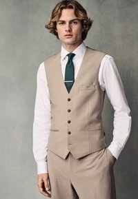 Gilet beige avec un col en V et cinq boutons, associé à une chemise blanche et une cravate vert foncé. Coupe ajustée, texture lisse et détails de poche latérale.