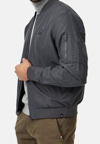 Grijze bomberjack met geribde kraag en manchetten, voorkant met rits, en zijzakken, voorzien van een ritszak op de arm en een soepele textuur.