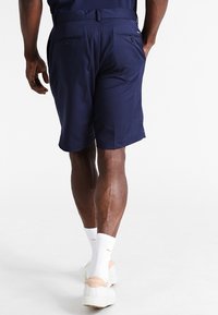 Marinblå shorts med skräddarsydd design, som har två bakfickor och en slät textur, kombinerat med vita strumpor och skor.