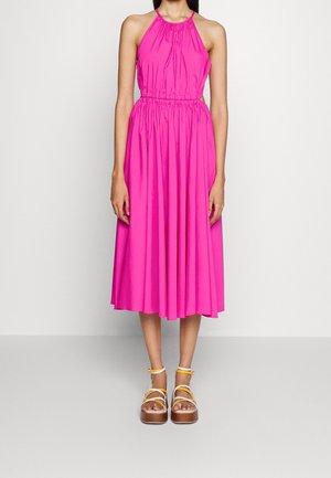 Kobieta w różowej, bezrękawnikowej sukience midi z marszczoną talią oraz białych sandałach na platformie z żółtymi paskami.