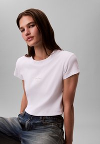 Lühikeste varrukatega valge soonikkoes T-särk, millel on rindkere piirkonnas peen Calvin Kleini logo, kombineeritud tuhmiks pleekinud siniste teksadega, sile tekstuur.