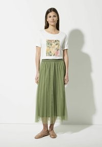 White t-shirt features a floral print with "my garden" text. Flowing green tulle skirt, textured and layered. Tan flats with embellishments.