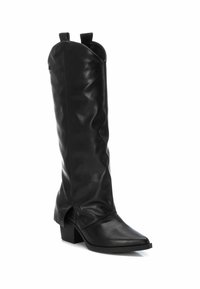 Bota de cuero negra hasta la rodilla con una textura suave, punta afilada y un tacón bajo tipo bloque. Cuenta con dos lengüetas en la parte superior para facilitar su colocación.