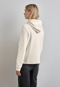 Felpa crema con tessuto testurizzato, dotata di cappuccio e polsini a coste, abbinata a pantaloni grigio scuro. Design semplice e rilassato.