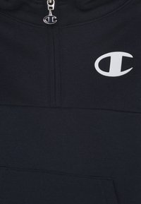 Tmavě modrá mikina s kapucí na zip z měkké látky, s klokaní kapsou a bílým logem na hrudi. Hladká textura s klasickým střihem.