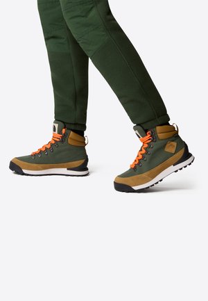 Stivali da trekking verdi con lacci arancioni, parte superiore in suede e tessuto, suola in gomma, collare alla caviglia imbottito e un logo distintivo sul lato.