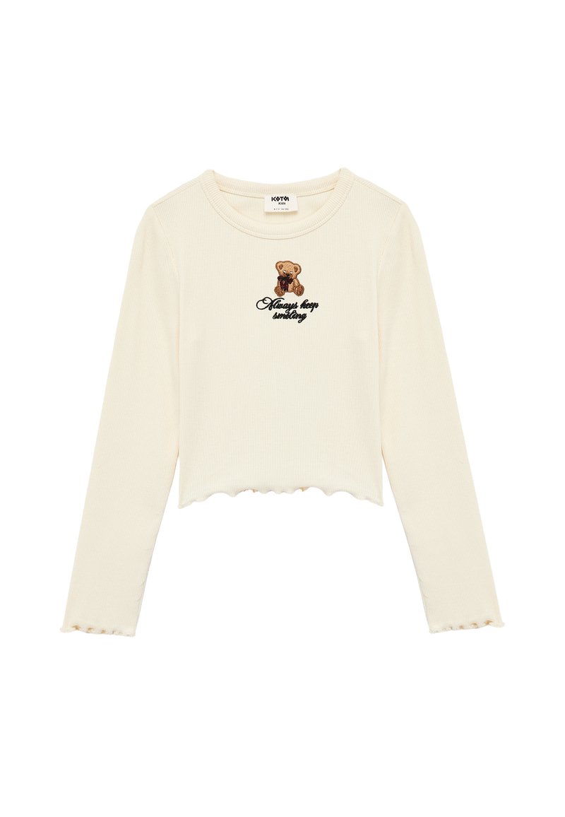 Top corto de manga larga color crema con dobladillo con ondas, que presenta un gráfico de un oso y la frase "Always keep smiling" bordada en negro. Material texturizado de canalé.