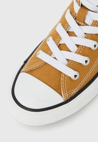 Πάνινο αθλητικό παπούτσι με μουσταρδί κίτρινο επάνω μέρος, λευκά κορδόνια και μύτη. Μαύρη καουτσούκ σόλα με υφασμένο σχέδιο στην άκρη.